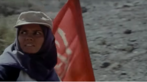 Figure 2: Maryam walking with the flag of the Basījīs she helps rescue. Still from The Survivors (Nijāt-yāftagān), directed by Rasūl Mullāqulīpūr, 1996.